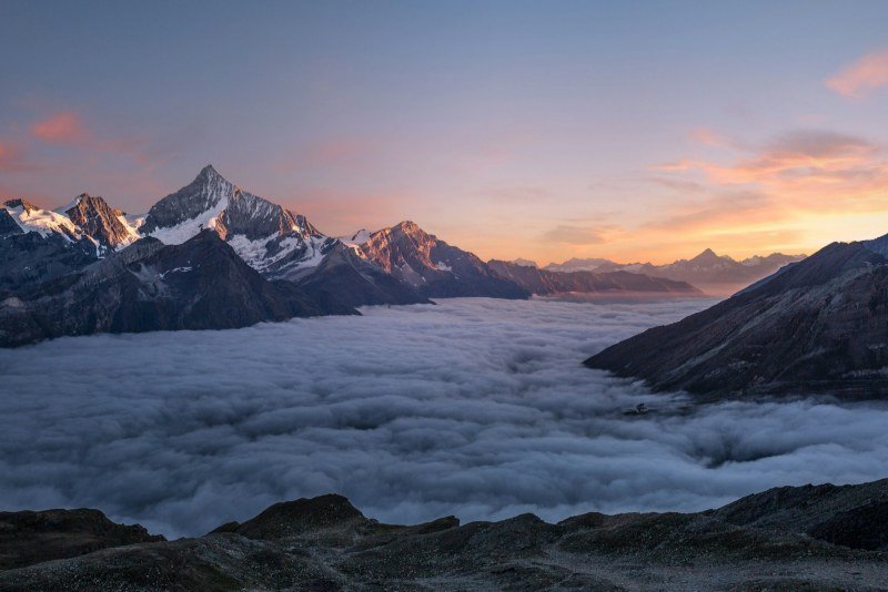 Snow-capped peaks above a sea of clouds at sunset