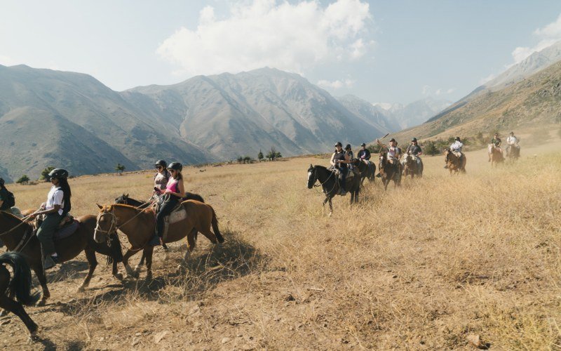 Riders in helmets crossing a golden Andes valley near Santiago, mountains behind