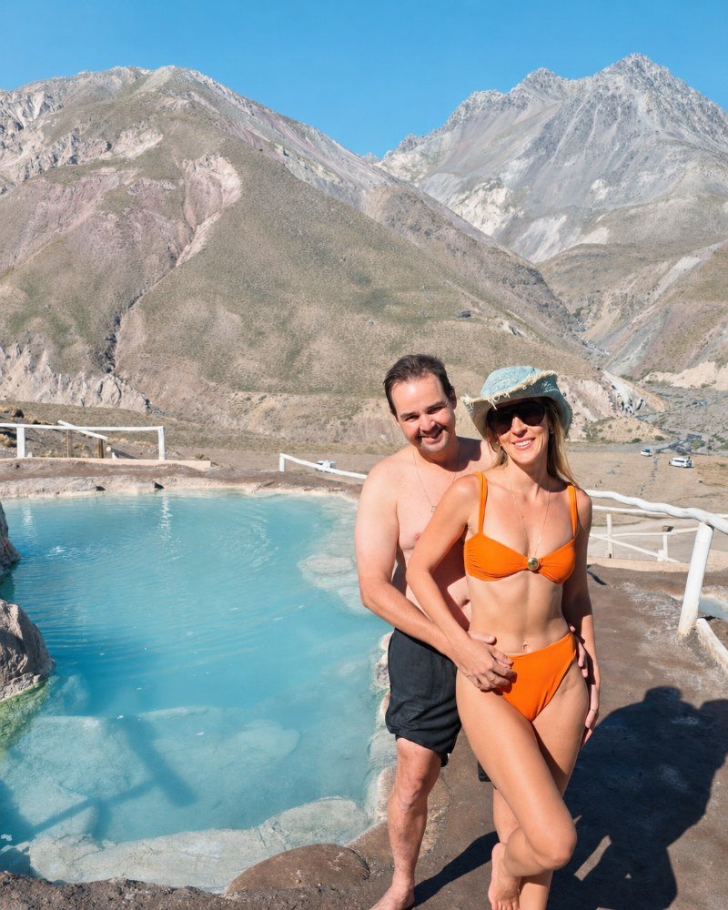 Couple relaxing in turquoise thermal pool with the volcanic Andes peaks rising behind them