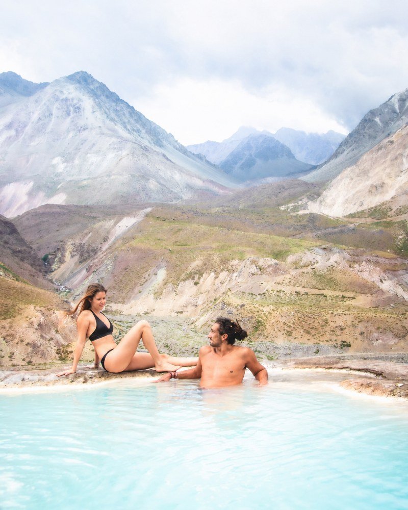 Couple relaxing at the edge of a thermal pool with a full panorama of the Andes behind them