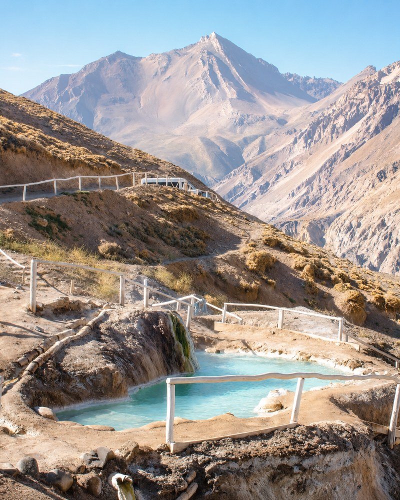 Thermal pools with a sharp volcanic peak rising steeply in the background